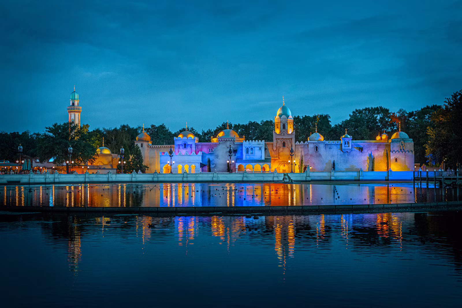 Efteling's Fata Morgana lit up across the lake at blue hour