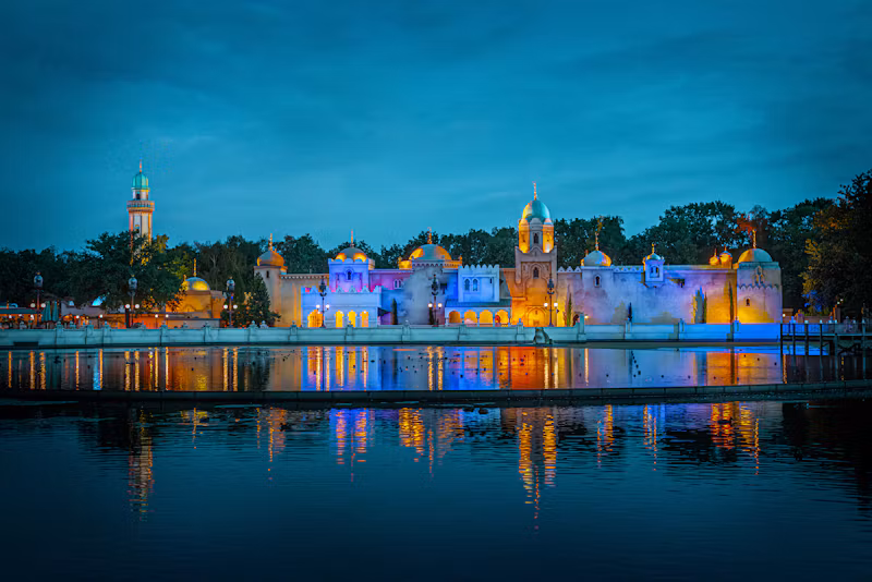 Efteling's Fata Morgana lit up across the lake at blue hour
