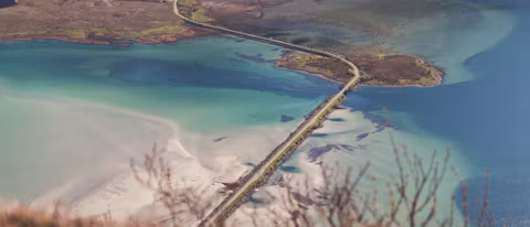 Aerial view of a coastal road crossing turquoise water in northern Norway