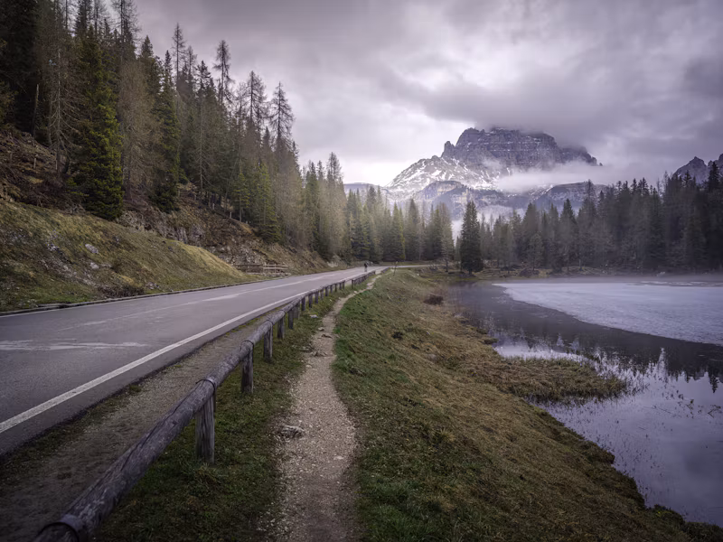 A mountain road beside a misty lake in the Dolomites, near Campitello di Fassa