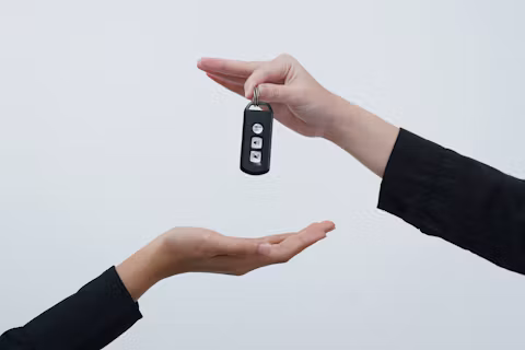 One hand passing a car key to another open hand against a pale background